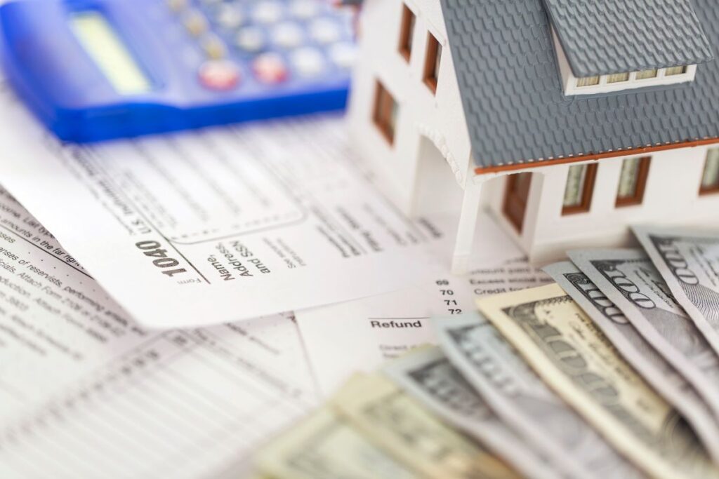 Photograph of tax forms, miniature house and money representing property tax. Arkansas Income Tax Rate article