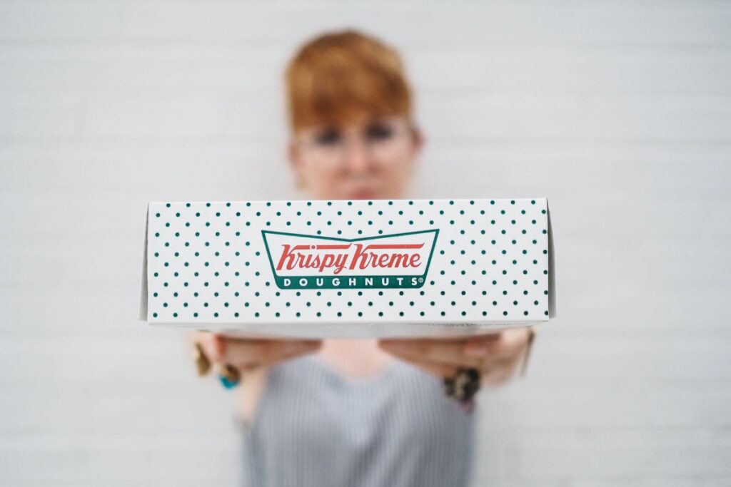 Who owns Krispy Kreme? Woman golding Krispy Kreme box