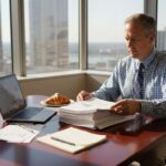 Financial advisor reviewing market reports in sunlit office - Finblog Financial advisor reviewing market reports in sunlit office