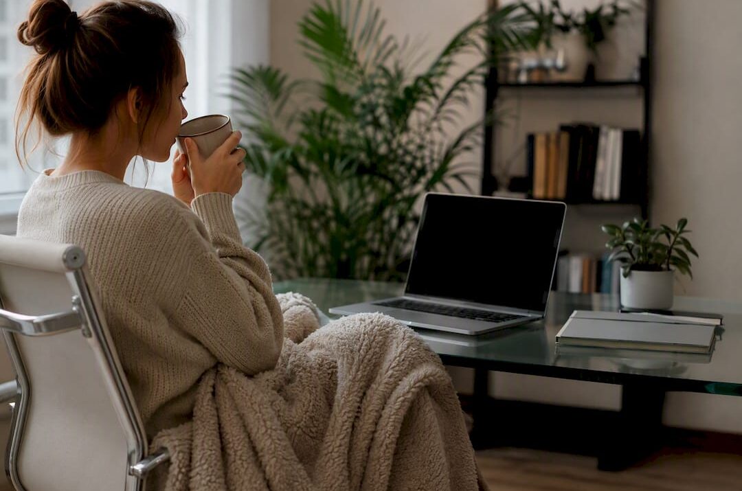 Hands wrapping blanket near tea on desk
