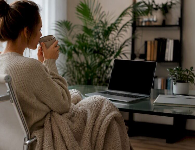 Hands wrapping blanket near tea on desk